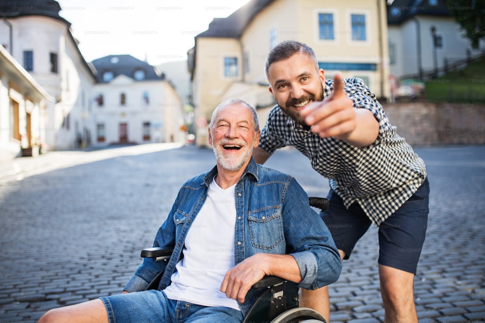 Un figlio hipster adulto con il padre anziano in sedia a rotelle durante una passeggiata in città, indicando qualcosa.