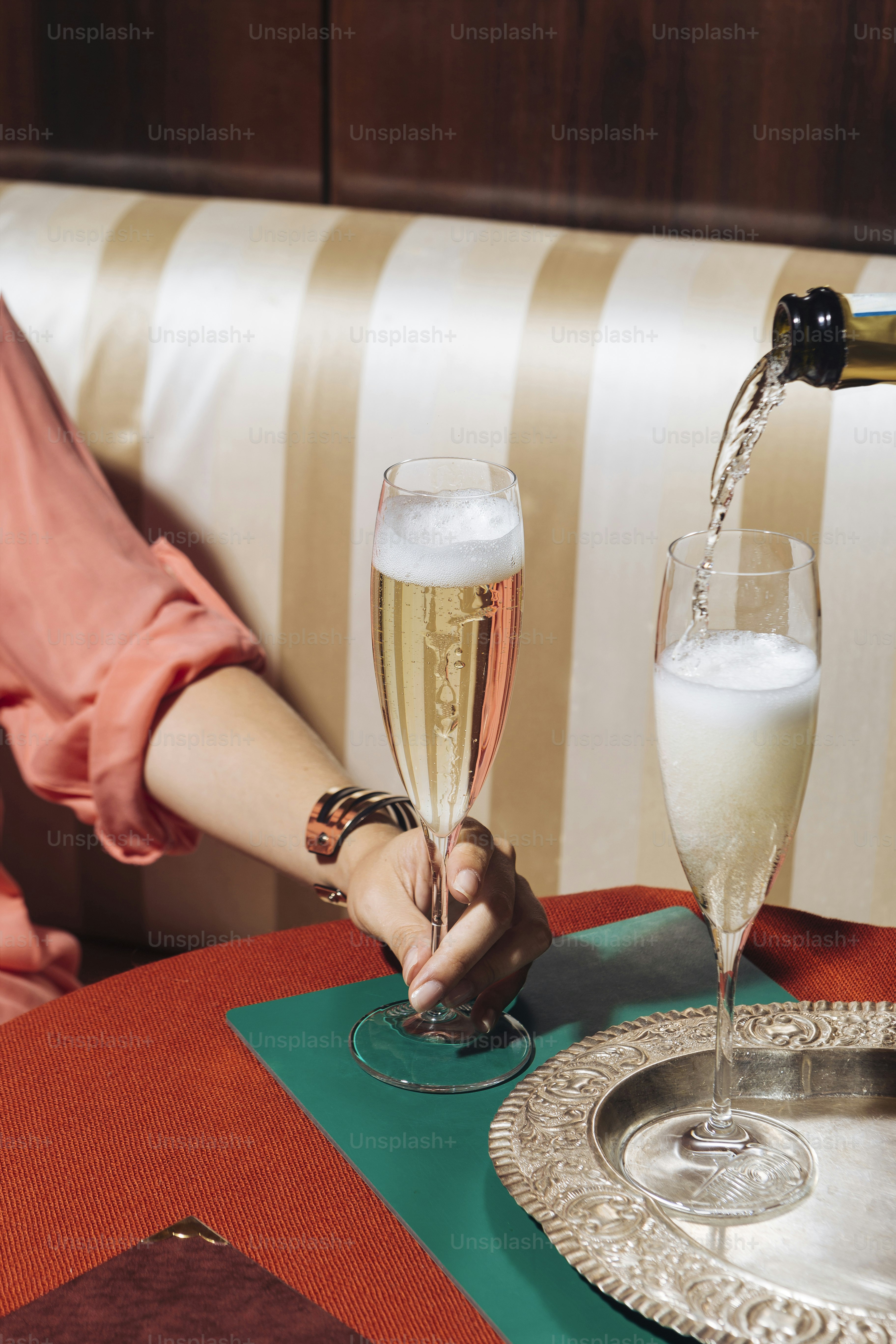 Un calice di prosecco tenuto in mano da una ragazza, in un elegante bar dai colori pop vintage