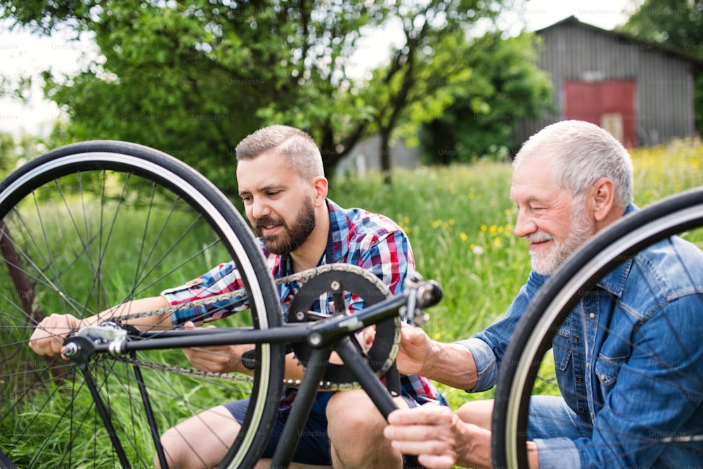 Un figlio hipster adulto e un padre anziano che riparano biciclette all'aperto in una soleggiata giornata estiva.