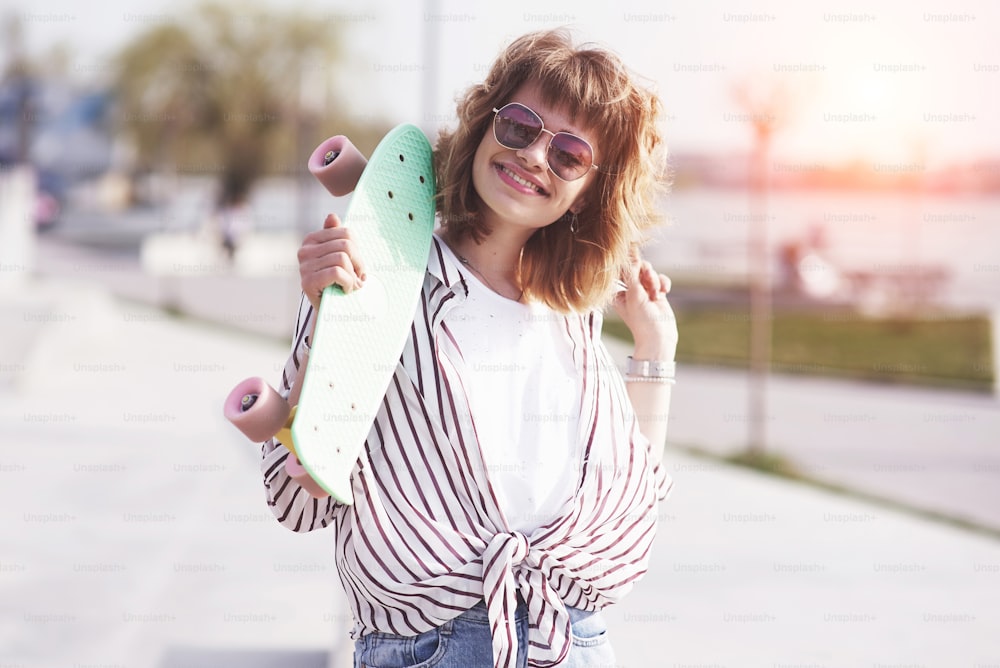 Beautiful teen female skater sitting on ramp at the skate park. Concept of summer urban activities.