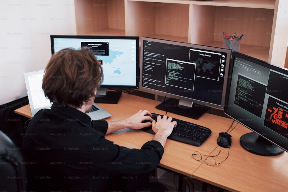 Il giovane e pericoloso hacker distrugge i servizi governativi scaricando dati sensibili e attivando virus. Un uomo usa un computer portatile con molti monitor.