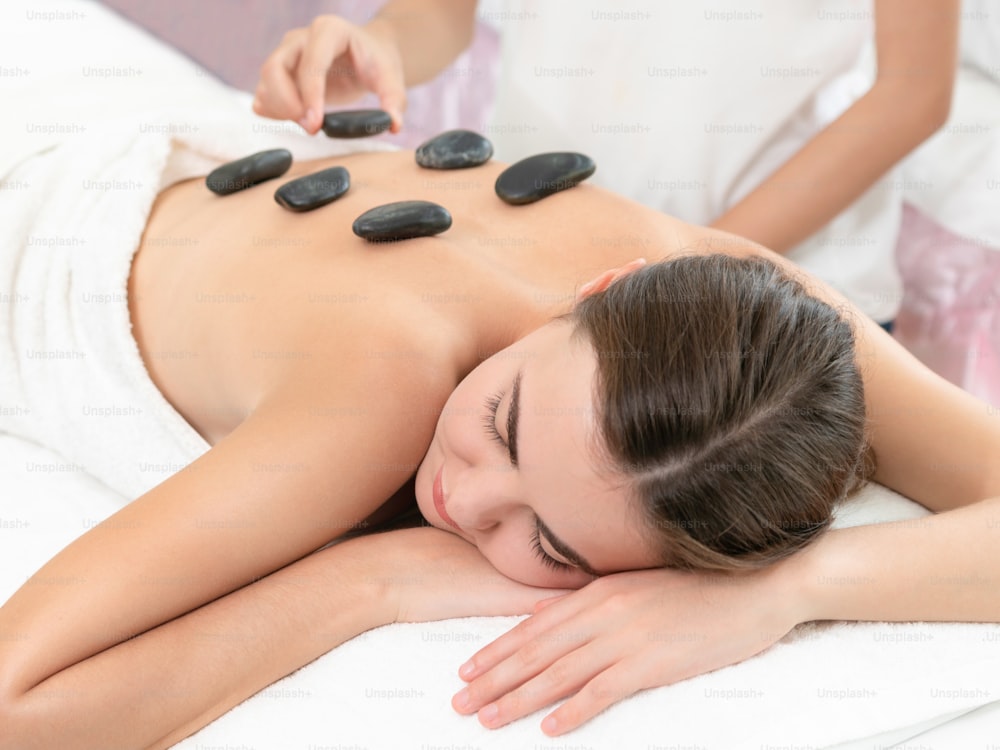 Frau, die eine Hot-Stone-Massagebehandlung von einer professionellen Kosmetikerin im Spa-Salon erhält. Luxus-Wellness-, Rückenstress- und Verjüngungskonzept.