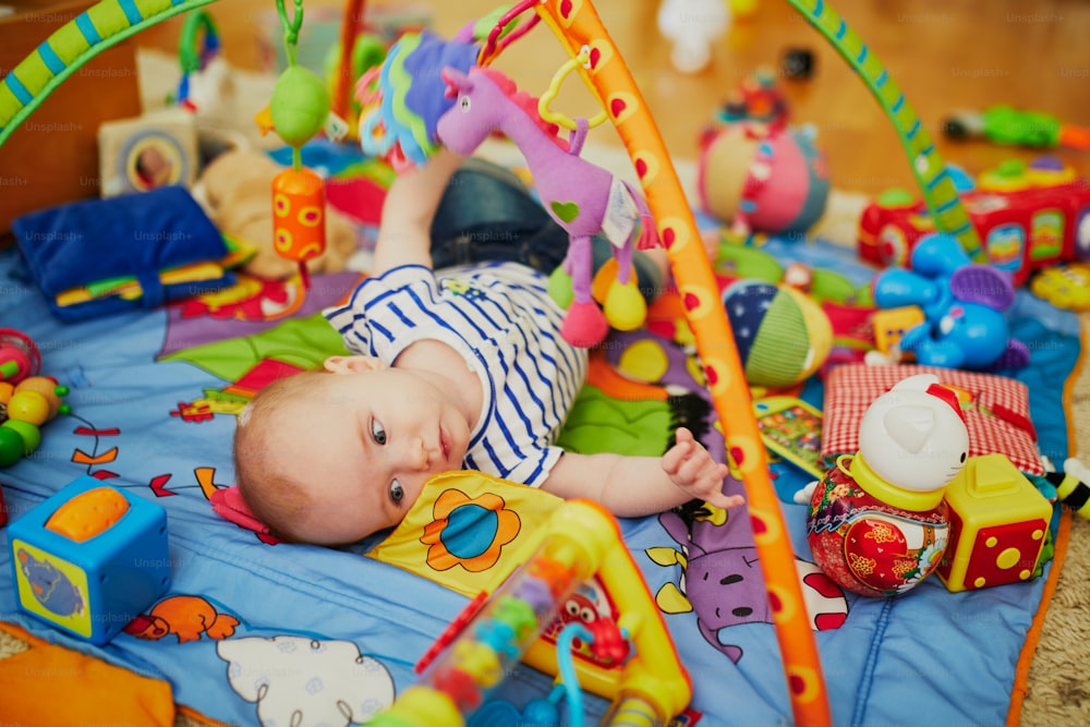 Baby girl with many colorful toys. Little child lying on playmat. Infant kid in nursery.