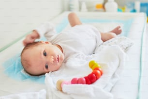 Newborn baby girl lying on changing table with wooden toy