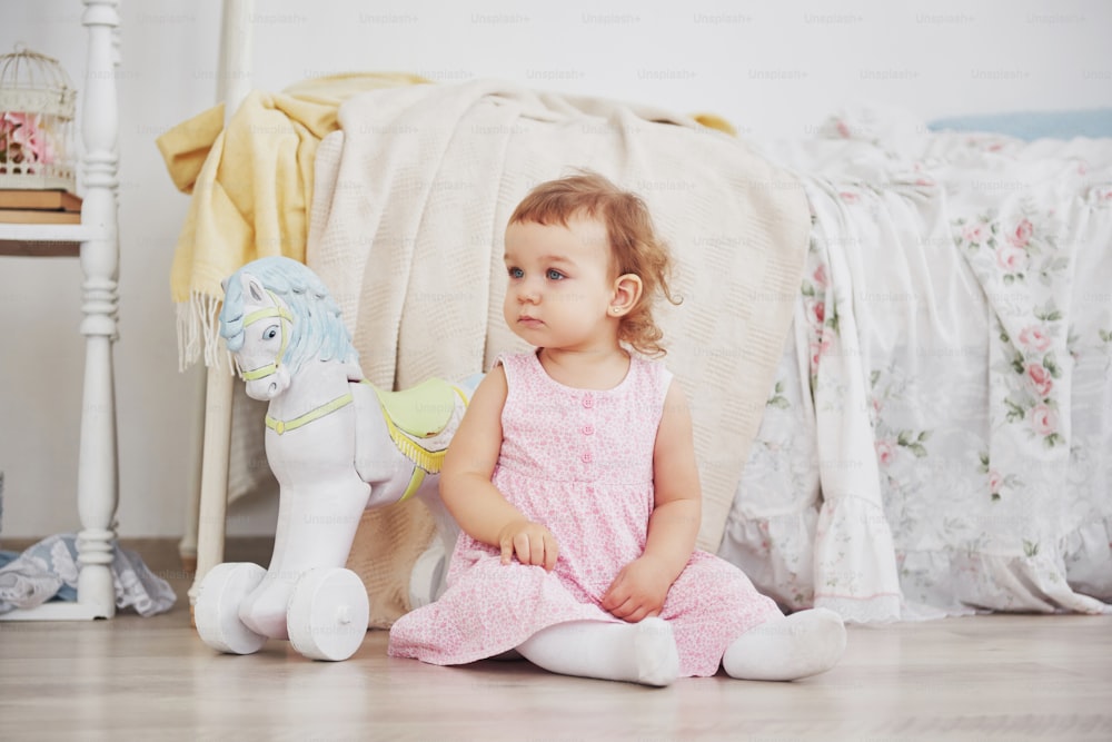 Hermosa niña jugando juguetes. Rubia de ojos azules. Silla blanca. Habitación infantil. Retrato de niña pequeña feliz. Concepto de infancia.