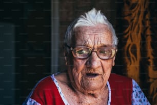 Porträt einer alten faltigen hundertjährigen Frau. Eine lächelnde Großmutter mit großer Brille. Alter, Freundlichkeit und Weisheit