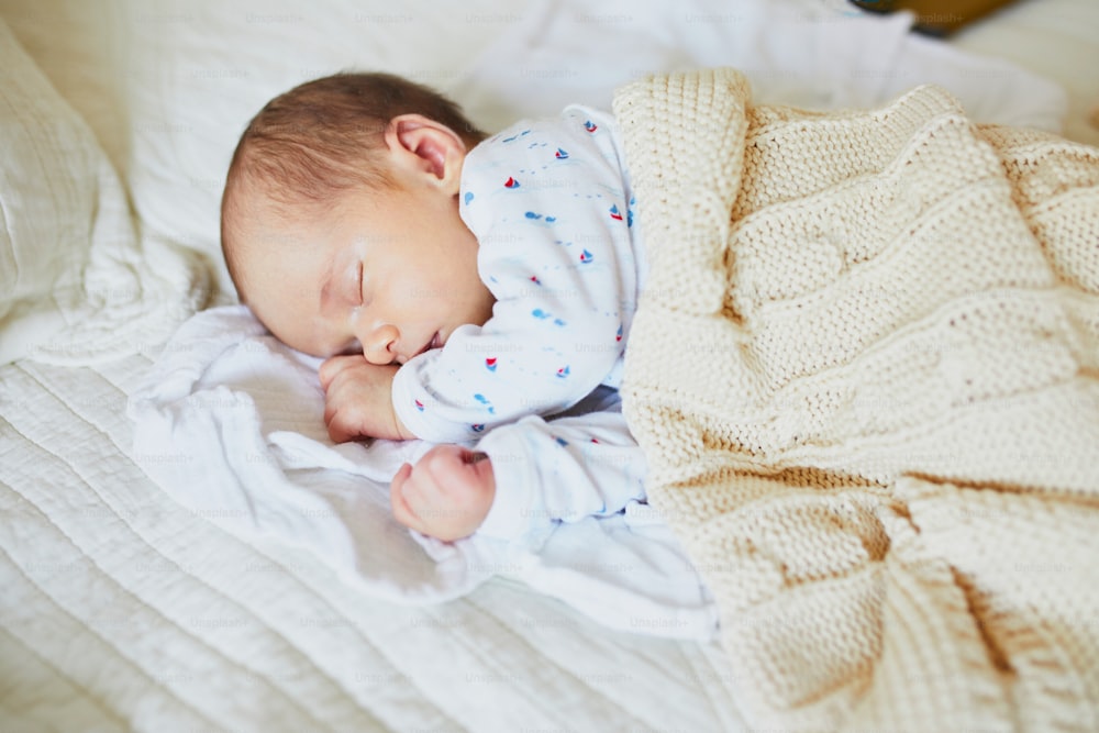 뜨개질 담요 아래에서 자고 있는 1개월 된 여자 아기. 부모의 침대에서 낮잠을 자는 아이