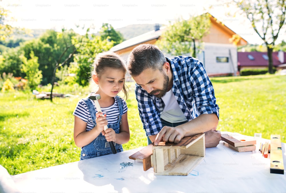 Father with a small daughter outside, making wooden birdhouse or bird feeder.