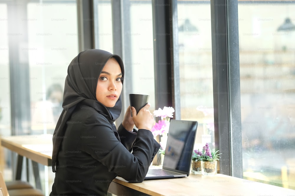 机の上のラップトップコンピュータで作業する魅力的な女性アラビア人企業員
