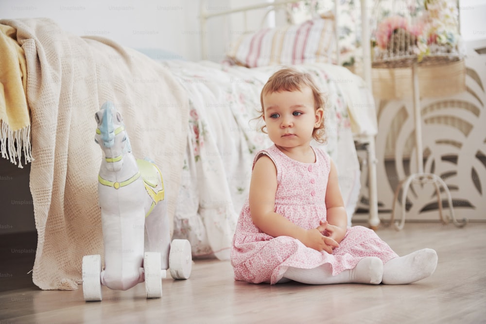 Beautiful little girl playing toys. Blue-eyed blonde. White chair. Children's room. Happy small girl portrait. Childhood concept.