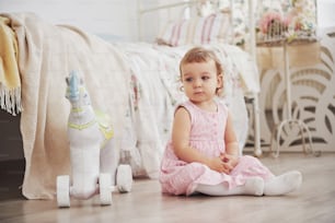 Schönes kleines Mädchen, das Spielzeug spielt. Blauäugige Blondine. Weißer Stuhl. Kinderzimmer. Glückliches kleines Mädchenporträt. Konzept der Kindheit.