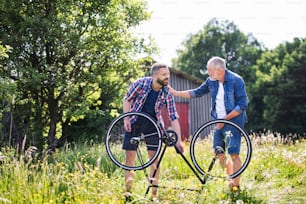 An adult hipster son and senior father repairing bicycle puncture outside on a sunny summer day.