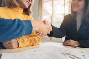 Happy young Asian couple and Real Estate Agent agent. Cheerful young man signing some documents and handshaking with broker while sitting at desk. Signing good condition contract.