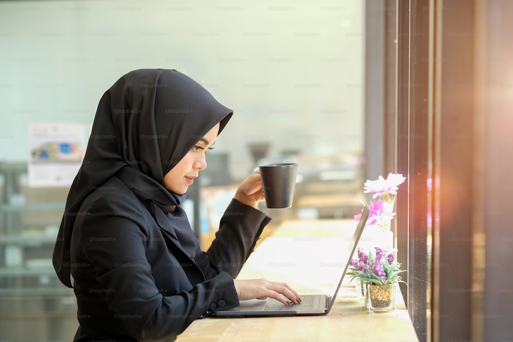 Árabe femenino atractivo que trabaja en una computadora portátil en el escritorio.