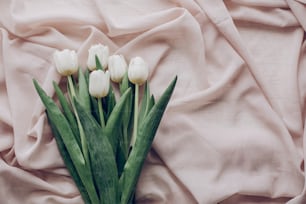 instagram spring flat lay. stylish white tulips on beige soft fabric on rustic table background top view. soft light, tenderness atmospheric moment. space for text. rustic wedding