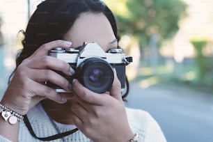 retrato da mulher jovem que se diverte tirando fotos com a câmera de filme retro. Retrato de estilo de vida ao ar livre.