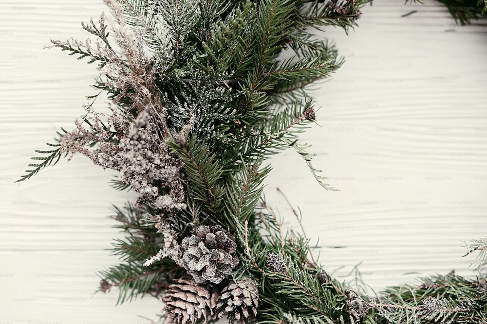 Couronne de Noël. Couronne de Noël rustique élégant sur porte en bois blanc avec des pommes de pin, des branches de sapin, de la neige. espace pour le texte. Décor fait à la main pour les vacances d’hiver.