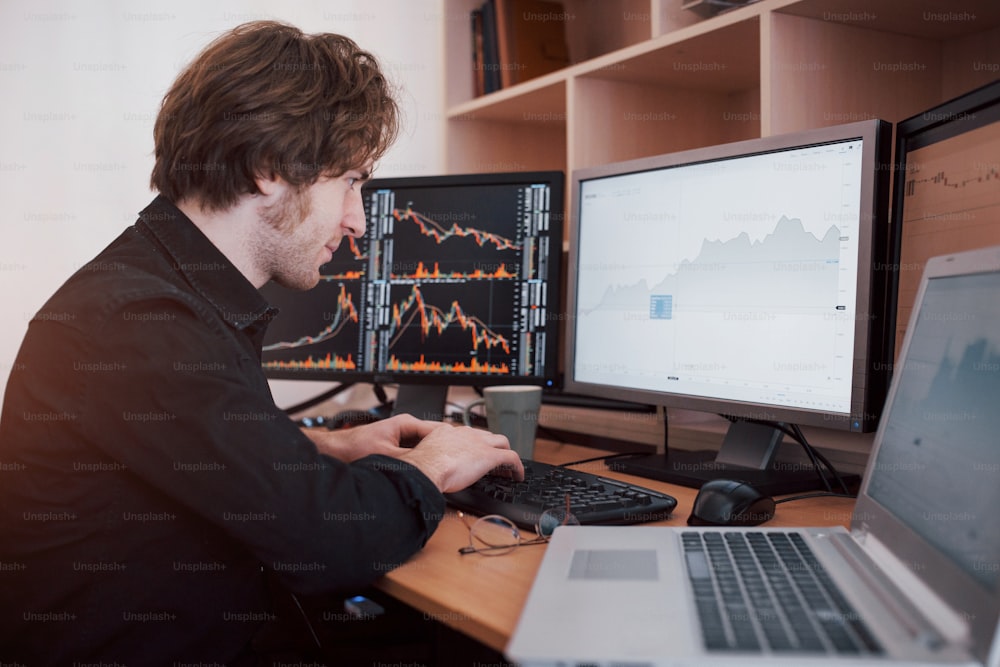Stressful day at the office. Young businessman holding hands on his face while sitting at the desk in creative office. Stock Exchange Trading Forex Finance Graphic Concept.