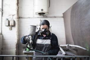 Mujer fuerte y digna haciendo un trabajo duro. Ella usa un compresor de pulverización industrial para pintar algunos productos metálicos.