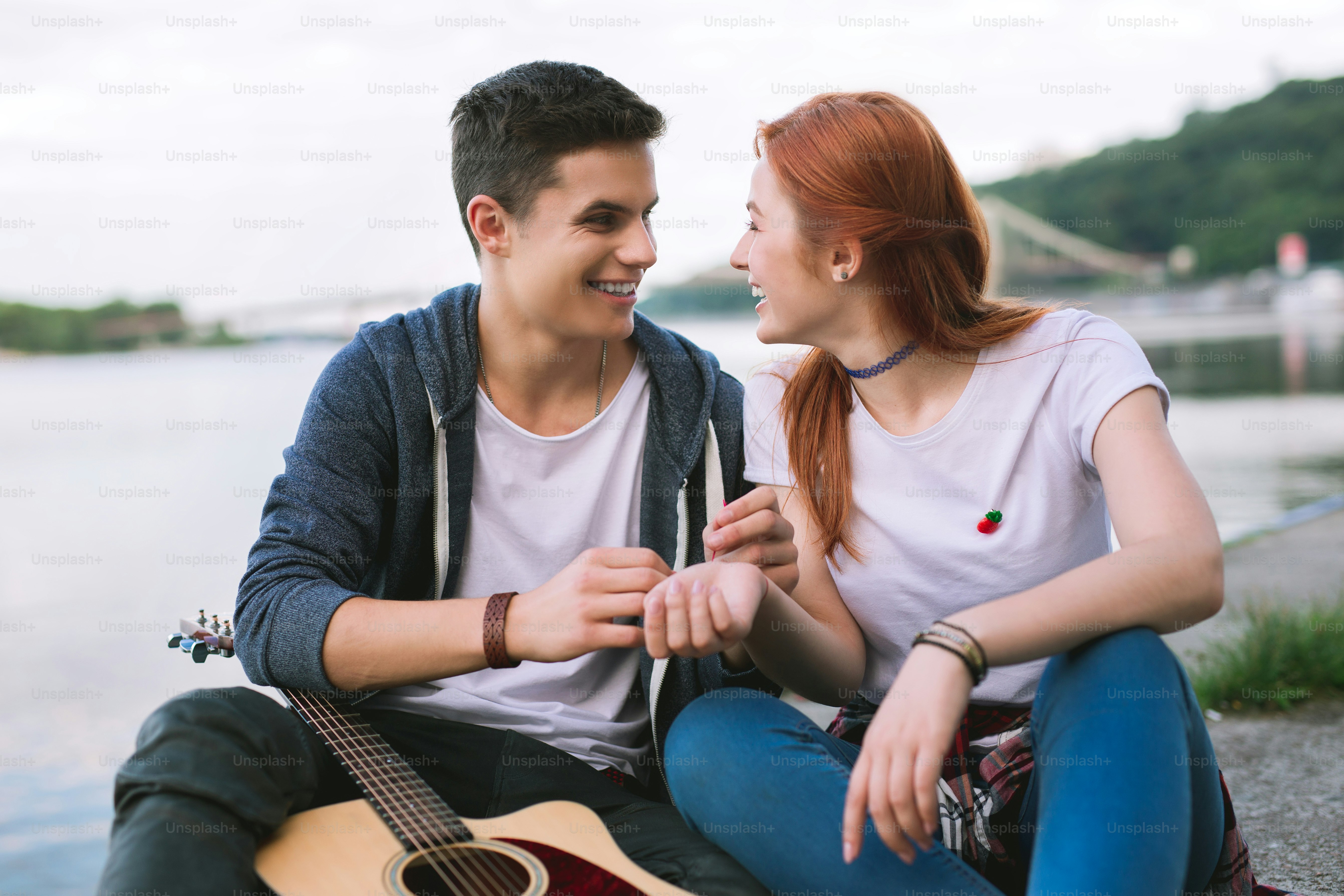 Junge Verliebte. Angenehm fröhliche Menschen, die sich gegenseitig anschauen, während sie zusammen am Fluss sitzen