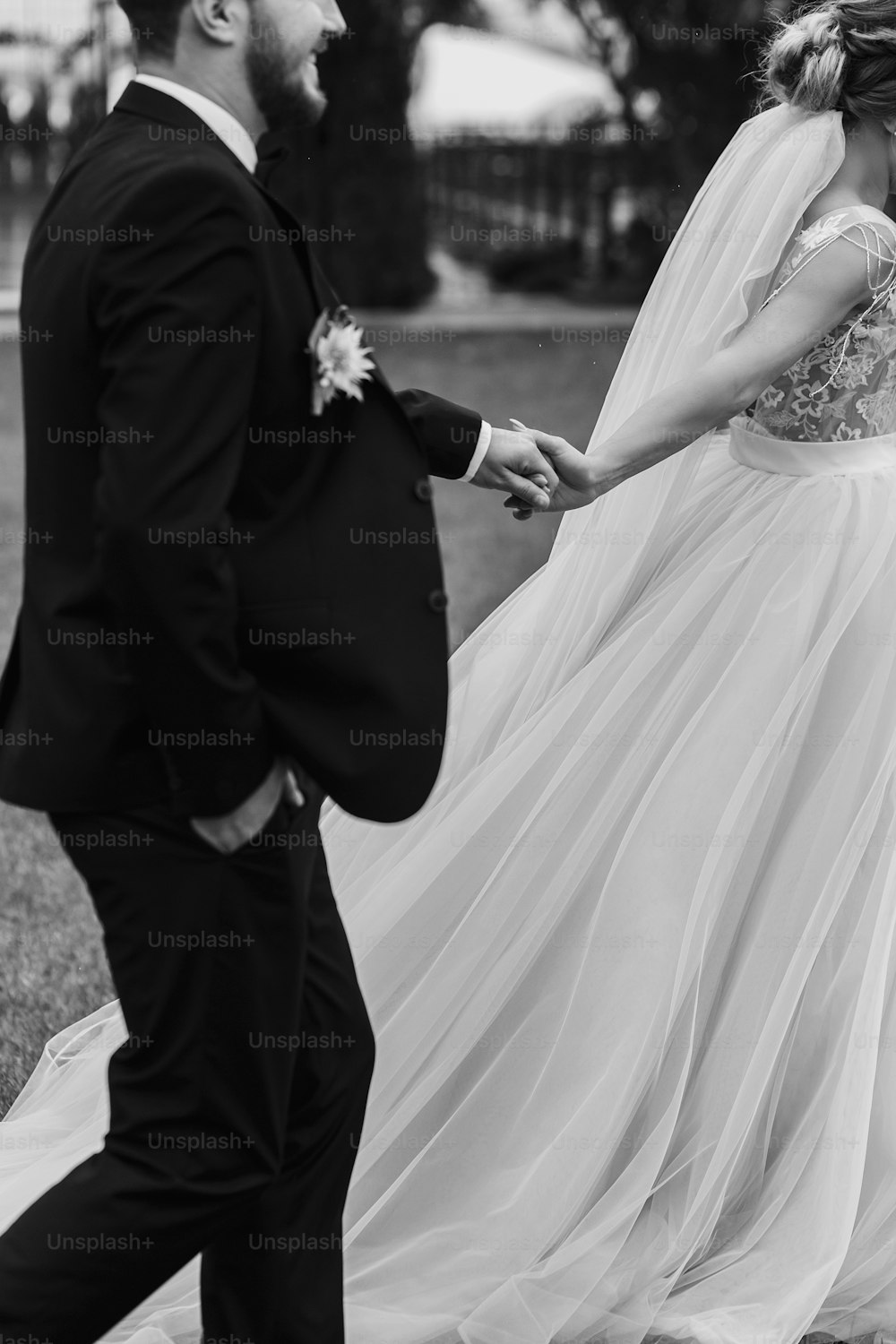 Wunderschöne Braut und stilvoller Bräutigam, die Händchen halten und im Freien spazieren gehen. Happy Sensual Hochzeitspaar umarmt. Romantische Momente des Brautpaares. Hochzeitsfoto