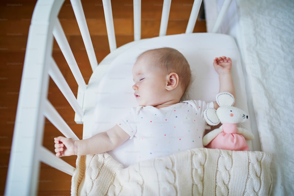 Adorable baby girl sleeping in co-sleeper crib attached to parents' bed. Little child having a day nap in cot. Infant kid in sunny nursery