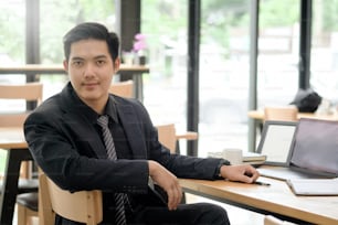 Retrato de un joven hombre de negocios asiático confiado en el escritorio de la oficina.
