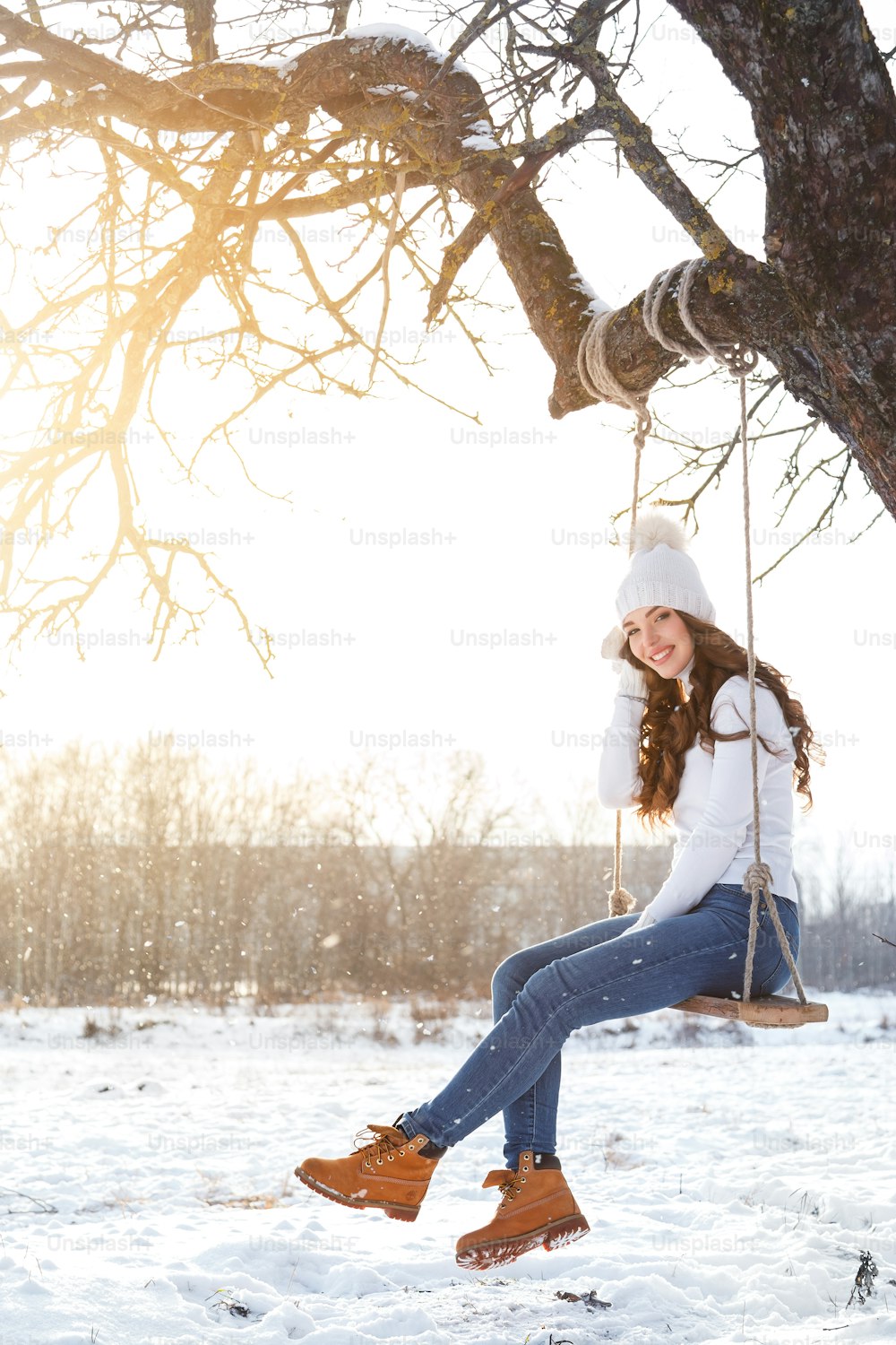 Muchacha feliz en el columpio de la cuerda en el día soleado de invierno