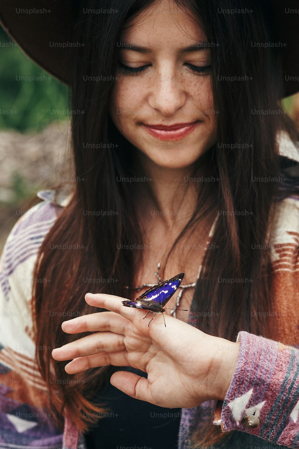 女の子の手に美しい蝶。スタイリッシュなヒップスター、山の森で指にアパチュラアイリスを握る帽子をかぶった幸せな女性。旅行と放浪癖のコンセプト。テキスト用のスペース。アメージング・モーメント