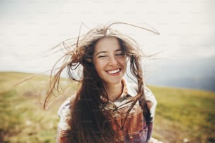 traveler hipster girl with windy hair and backpack, standing on top of sunny mountains. space for text. stylish woman waving hair. atmospheric moment. travel and wanderlust concept.