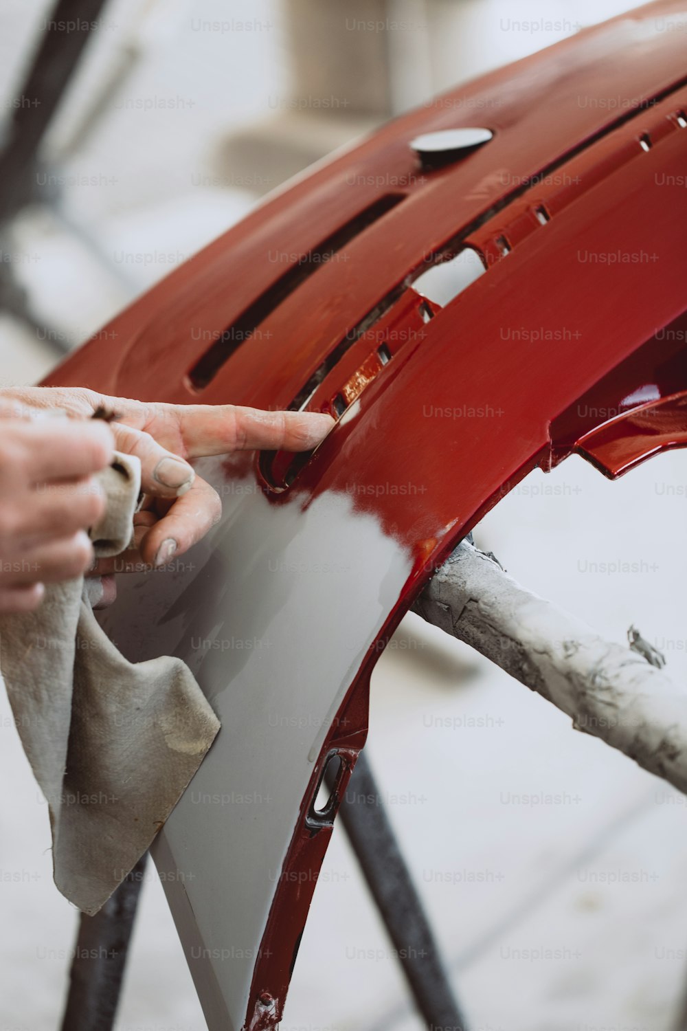 Autodetaillierung - Mann mit Schleifpapier in der Autowerkstatt schleift Polieren und Vorbereiten von Autoteilen für die Lackierung. Selektive Fokussierung auf die Hand des Menschen.