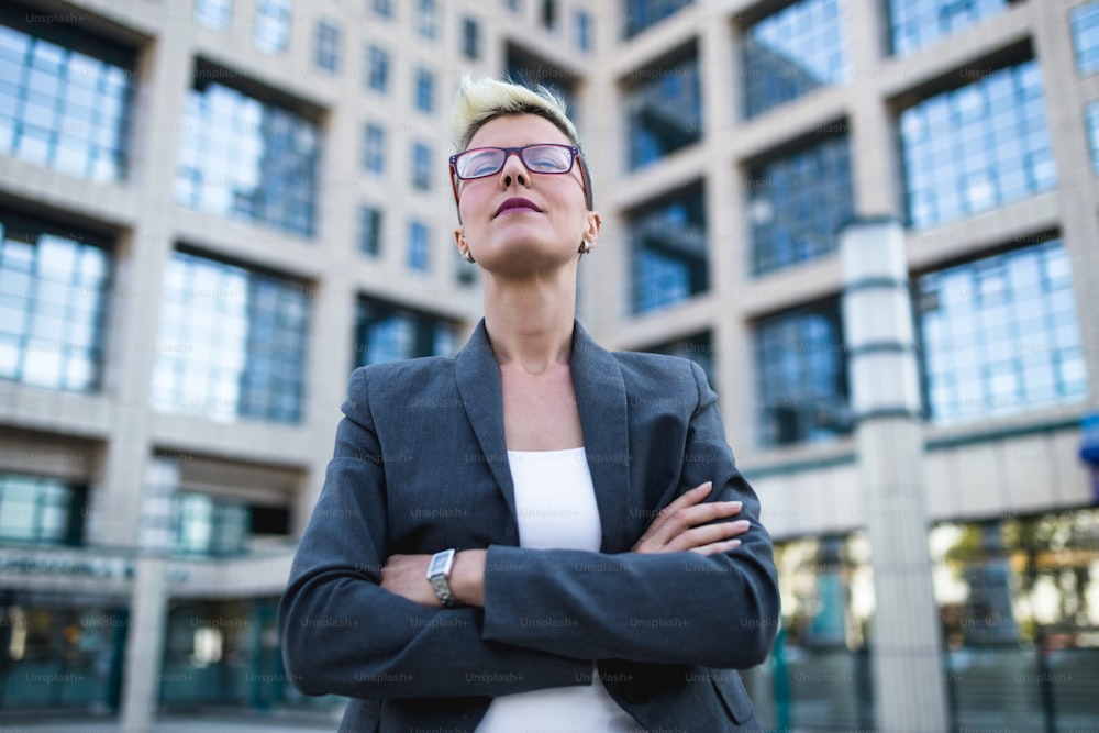 Portrait of serious and confident business woman standing in front of big modern building. Low angle view.