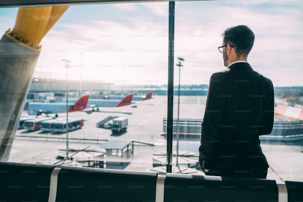 Schiena di un giovane uomo d'affari in piedi con la valigia all'aeroporto in attesa del volo