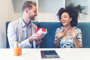 Feliz pareja interracial de mediana edad sentada en el bar del café, sonriendo y mirando la tableta blanca.