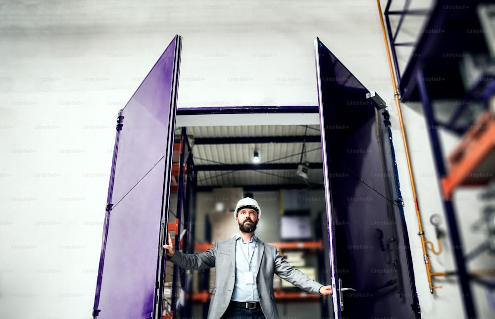 Un ingénieur industriel avec une veste dans une usine, ouvrant et franchissant la porte.