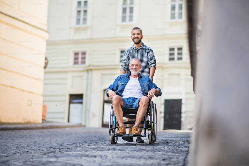 Un fils hipster adulte avec son père aîné en fauteuil roulant lors d’une promenade en ville.