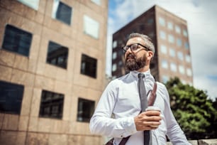 Hipster businessman with bag and coffee standing on the street in London. Copy space.