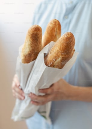 Cropped vertical photo of young woman in blue uniform shirt stand half turn isolated on pastel background made manufacture, aromatic, perfect hot bread, hold it in hands focus on gold crust baguettes