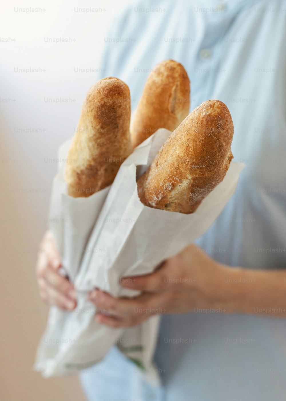Cropped vertical photo of young woman in blue uniform shirt stand half turn isolated on pastel background made manufacture, aromatic, perfect hot bread, hold it in hands focus on gold crust baguettes