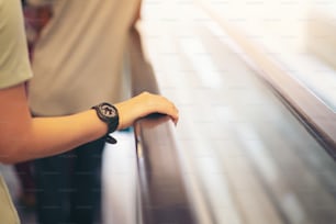 Point de vue d’une femme empruntant un escalator jusqu’au deuxième étage du centre commercial. Une main visible dans le cadre qui maintient le rail de l’escalator.