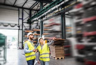 A portrait of a mature industrial man and woman engineer with tablet in a factory, working.