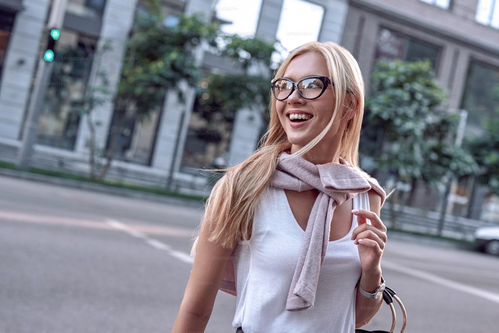 Profile of a beautiful businesswoman with glasses and handbag. She crosses the road and smiling