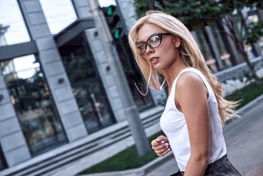 Profile of a beautiful businesswoman with glasses and handbag. She crosses the road and looks for cars nearby