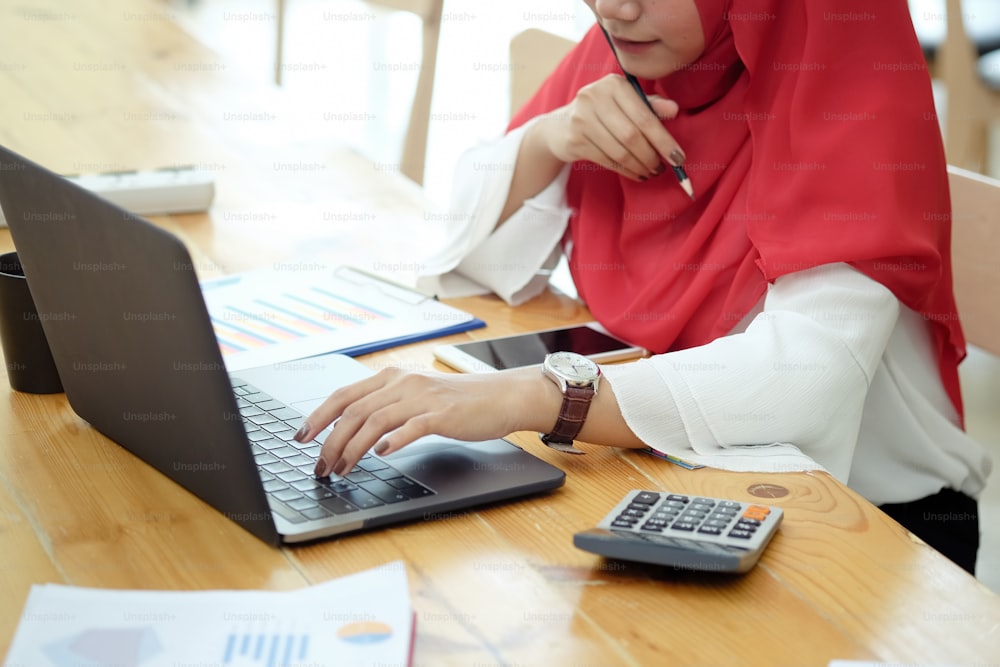 Árabe feminino atraente que trabalha no computador portátil e papelada na mesa