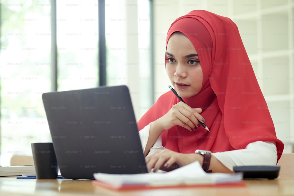 Attractive female Arabic working on laptop computer and paperworks on desk