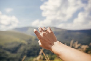 婚約指輪で山に手を差し伸べる旅人の手。日当たりの良い山々と空の背景に女の子の手。旅行と放浪癖のコンセプト。夏休み