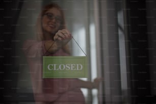 Store owner turning closed sign In shop doorway.