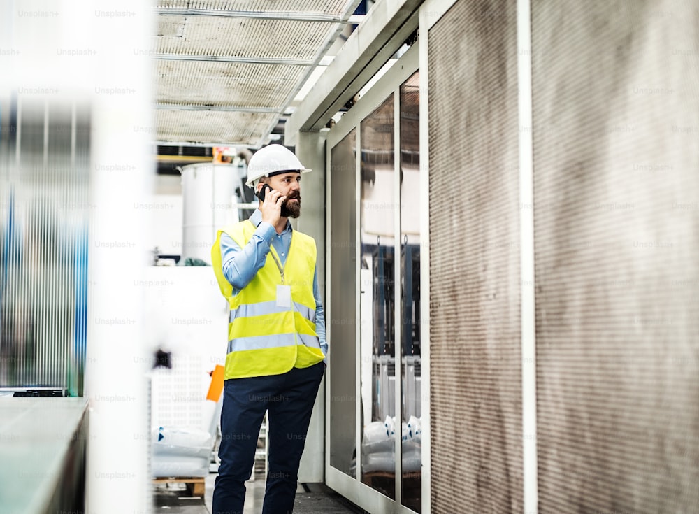 A portrait of a mature industrial man engineer with smartphone in a factory, making a phone call.