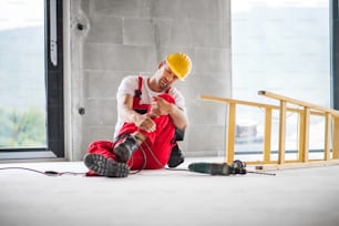 An accident of a male worker at the construction site. A man with an injured leg sitting on the floor.