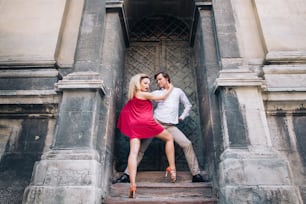 Hermosa pareja feliz enamorada abrazada y bailando en el viejo edificio de la calle soleada. elegante novio hipster y novia rubia en vestido rojo realizando baile, bailarines profesionales. Momentos románticos